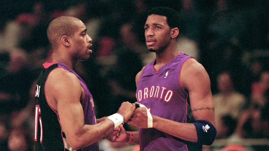 On April 23, 2000, Vince Carter #15 of the Toronto Raptors shakes hands with teammate Tracy McGrady #1 during round one of the NBA Playoffs against the New York Knicks at the Madison Square Garden in New York. The Knicks defeated the Raptors 92-88. Image taken by Ezra O. Shaw and sourced from Getty Images.