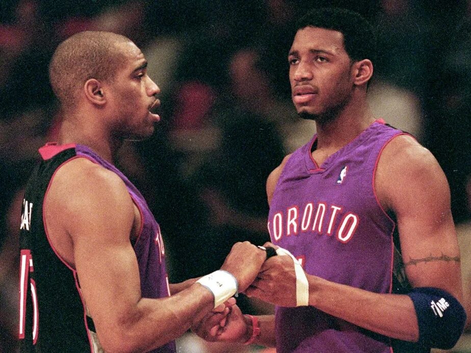 On April 23, 2000, Vince Carter #15 of the Toronto Raptors shakes hands with teammate Tracy McGrady #1 during round one of the NBA Playoffs against the New York Knicks at the Madison Square Garden in New York. The Knicks defeated the Raptors 92-88. Image taken by Ezra O. Shaw and sourced from Getty Images.