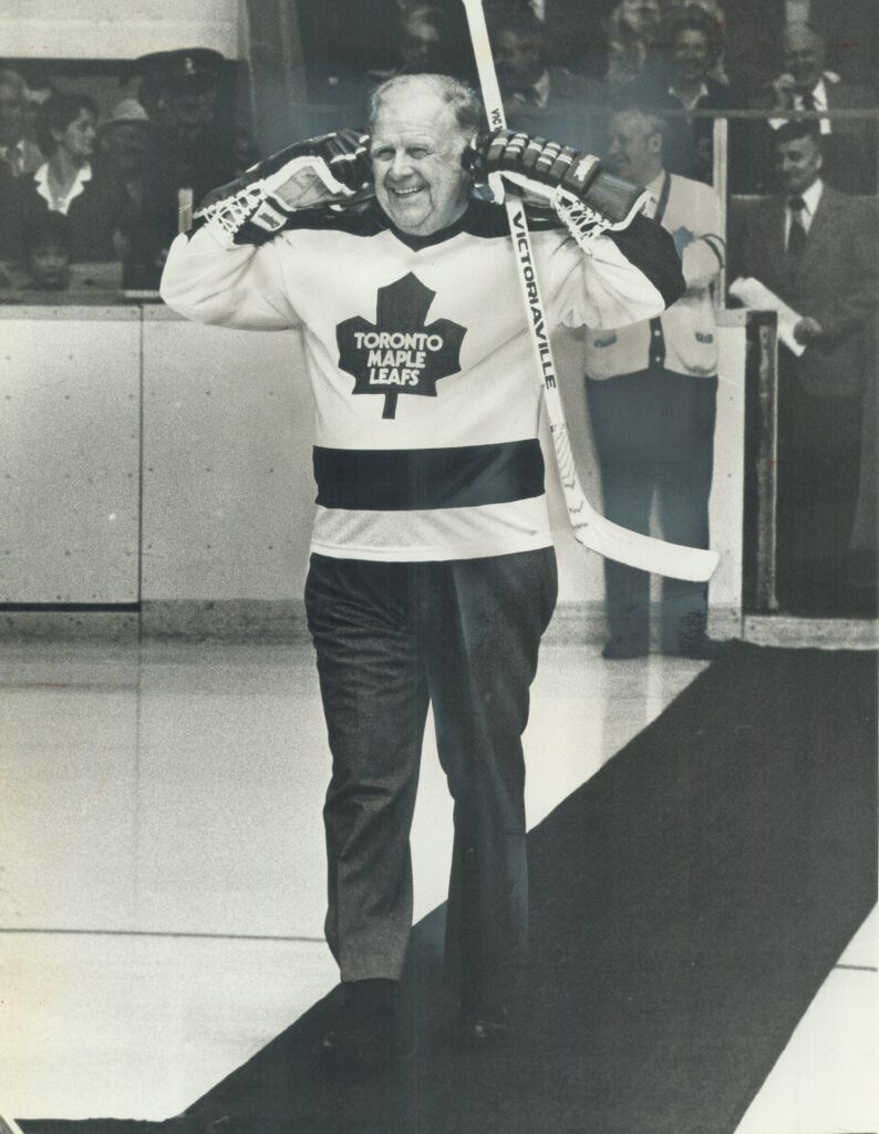 A photograph of Harold Ballard in a Maple Leafs jersey trying to jokingly block out the sound of jeering crowds. The Toronto Star article headline for this image, published on March 23, 1980, reads: "Trade him: Fans expressed their love -- in jeers -- for Leafs' boss Harold Ballard na old-timers' game last night." Image taken by Jeff Goode and sourced from the Toronto Public Library.