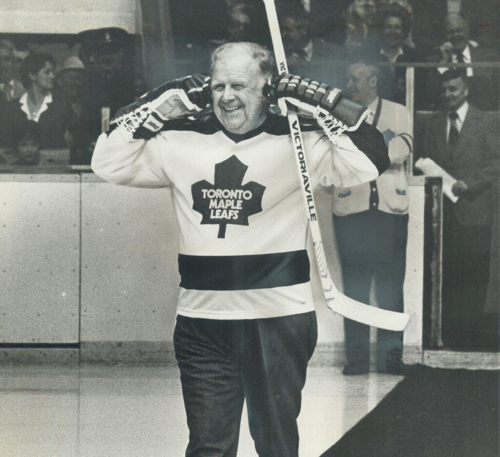 A photograph of Harold Ballard in a Maple Leafs jersey trying to jokingly block out the sound of jeering crowds. The Toronto Star article headline for this image, published on March 23, 1980, reads: "Trade him: Fans expressed their love -- in jeers -- for Leafs' boss Harold Ballard na old-timers' game last night." Image taken by Jeff Goode and sourced from the Toronto Public Library.