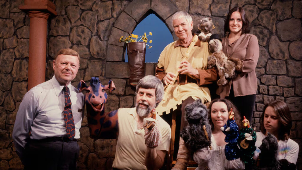 The Friendly Giant contributors, including harpist John Duncan, puppeteer Rod Coneybeare with Jerome the Giraffe and Rusty the Rooster, puppeteer Nikki Tilroe, puppeteer Karen Valera, creator Bob Homme, and puppeteer Nina Keogh. Image captured on September 18, 1982 and sourced from the CBC.