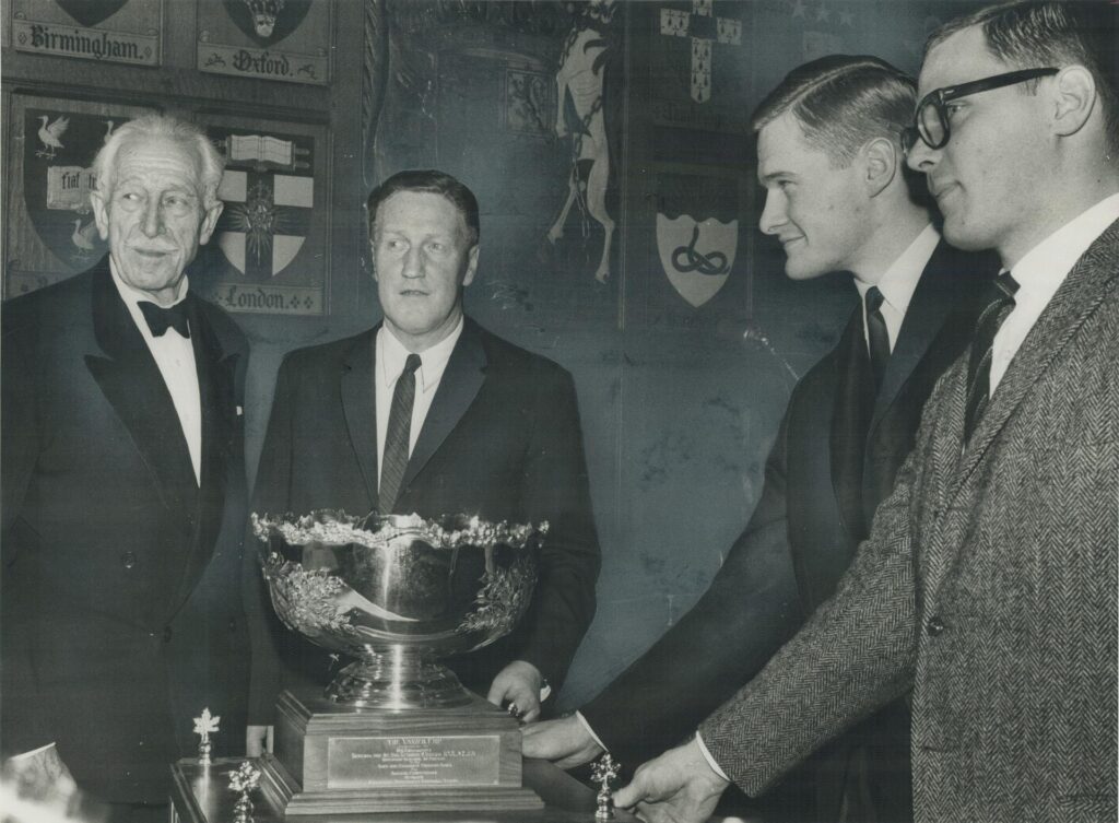 A photograph of Governor-General George Vanier (left) presents Vanier Cup to Varsity Blues; winners of College Bowl game. Receiving award are: (left to right) former coach Dalt White and Varsity's co-captains Bryce Taylor and Bob Pampe. Originally from taken for a Toronto Star article. Photographed by Doug Griffin and sourced from the Toronto Public Library.