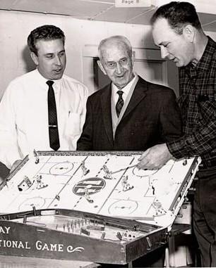 A photograph of Donald H Munro Jr.; Donald H Munro, and William M Munro looking at one of their original 1935 models of a table hockey game, taken in 1967. Image sourced from Clan Munro Association.