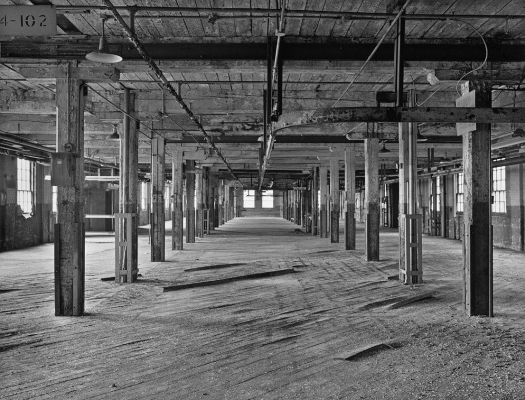 A black-and-white photograph of an abandoned Massey Ferguson factory interior.